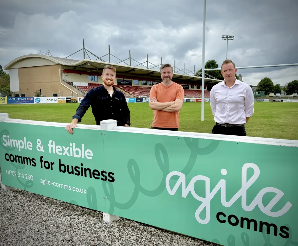 Ollie Jackman and James Fisher - Agile Directors and Founders - pictured with James Greenacre - Head of Commercial at Plymouth Albion RFC - next to the Agile Comms sponsorship board at the ground.