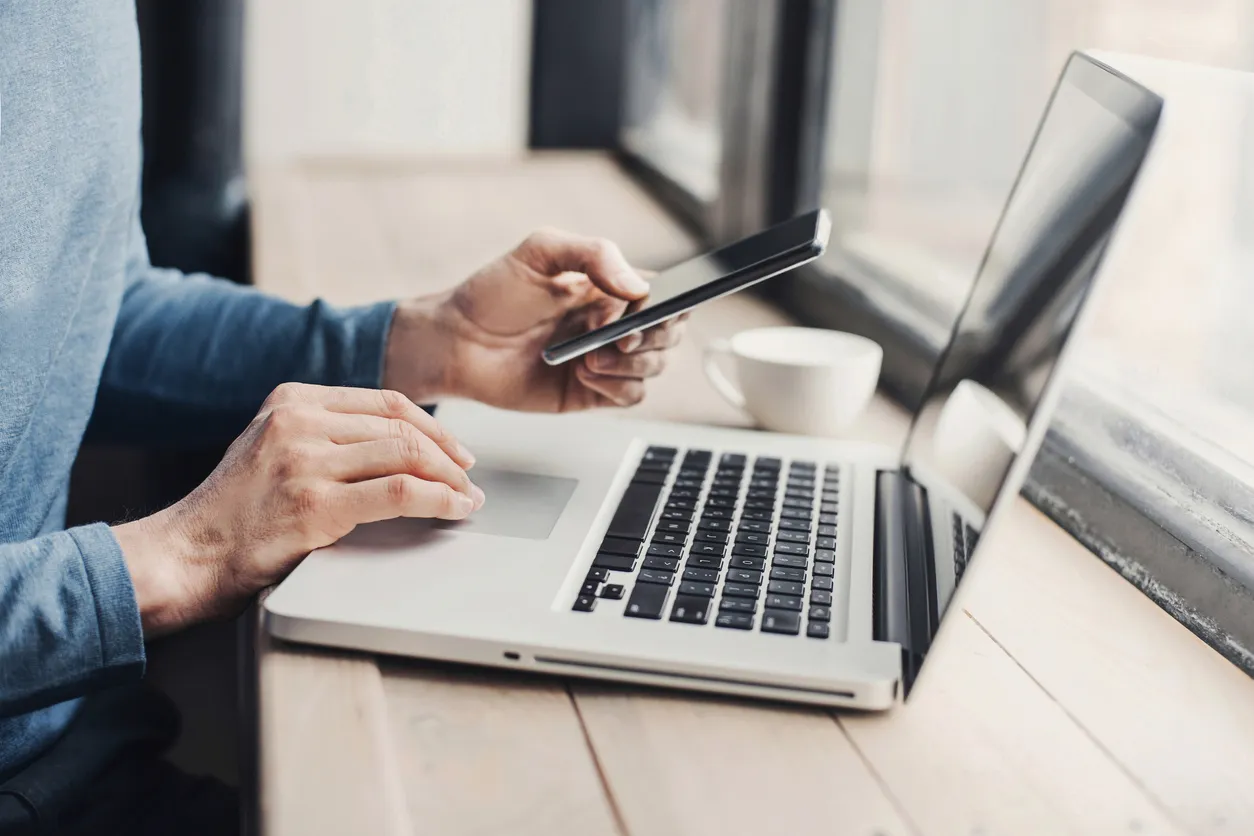 Person typing on laptop and using smartphone
